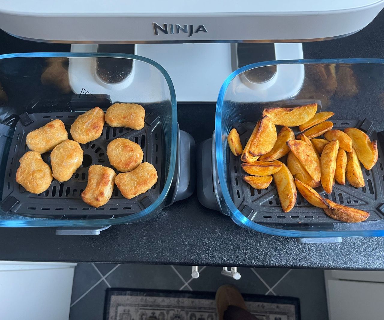 Two glass air fryer baskets pulled out with cooked chicken nuggets in one and fries in the other