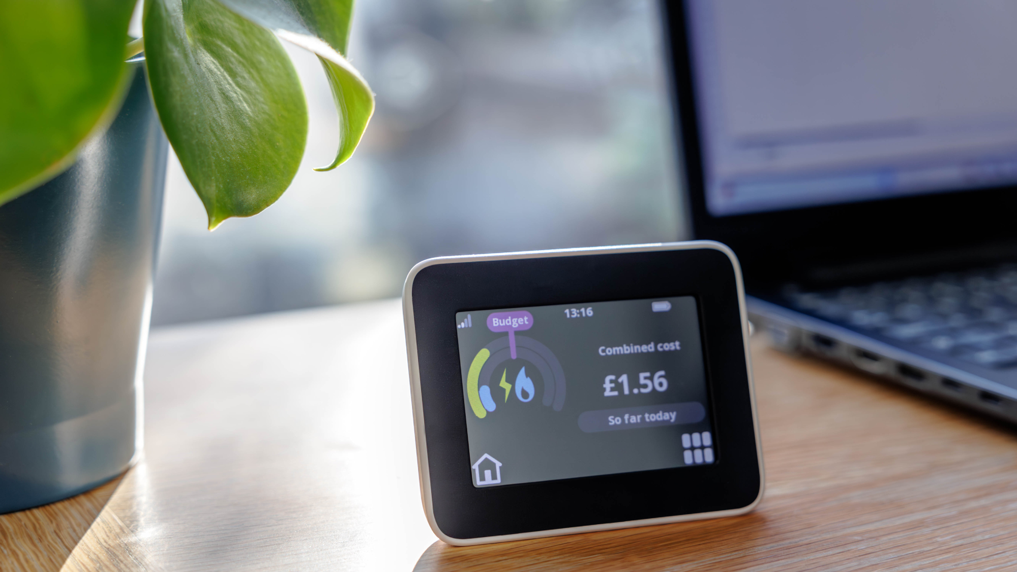 smart energy meter on desk next to laptop and plant in silver pot
