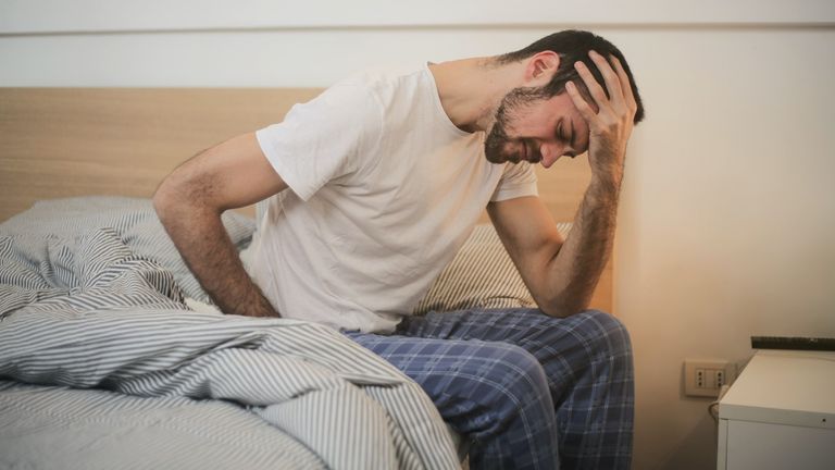 Man sitting on a bed in discomfort