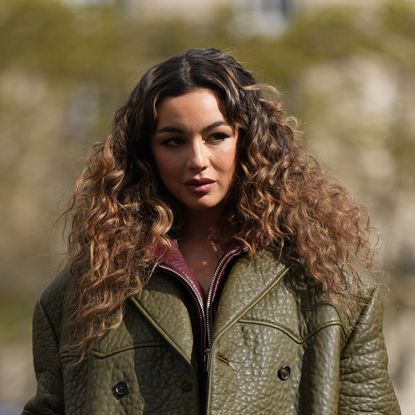 best straightener for curly hair - A woman with curly hair walking down the street wearing green oversized winter leather jacket with texture and burgundy lining 