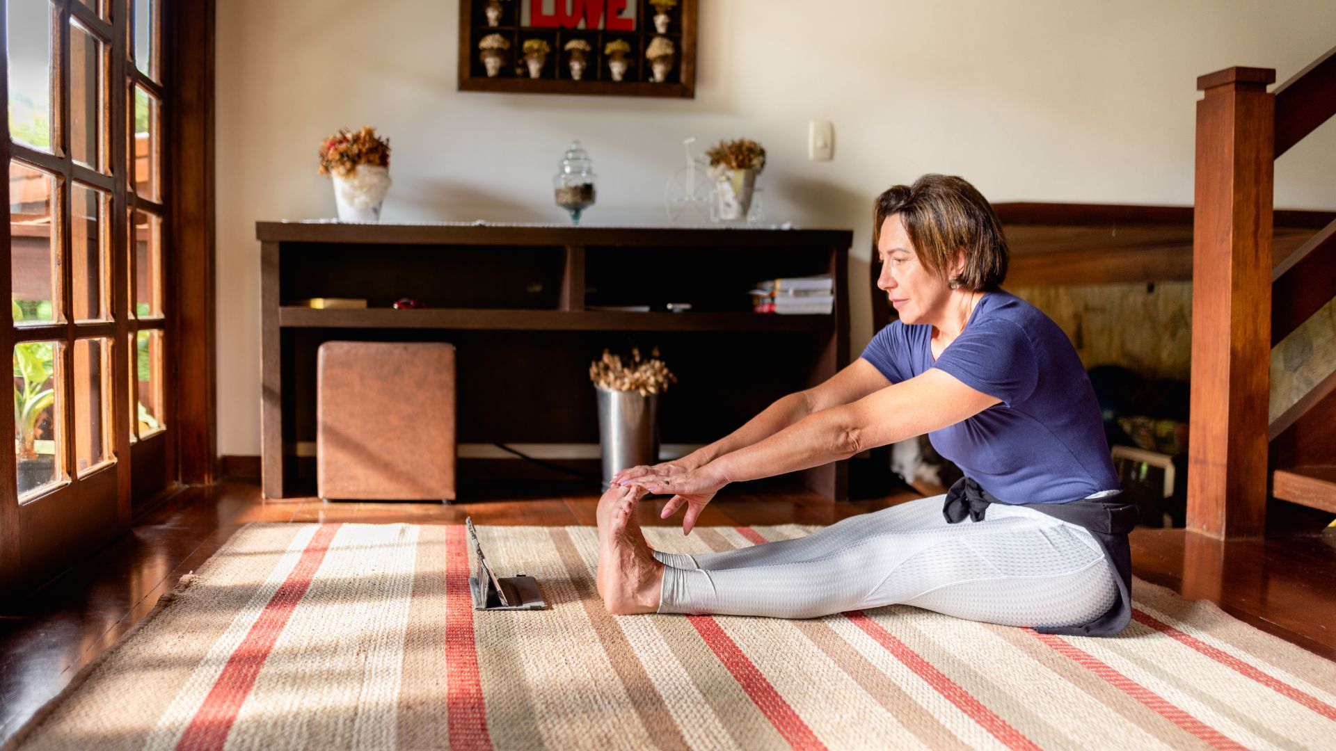 Woman warming up at home to do weight-bearing exercises for osteoporosis with tablet on stand to watch video