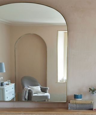 A pink living room with a gold arched mirror reflecting the room