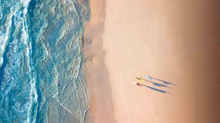 Drone shot of three people with long shadows on a beach