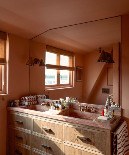 Bathroom with Naperon by Farrow & Ball painted walls, a wooden double vanity unit with a red marble top, and a large mirror with two brass sconces on either side. 
