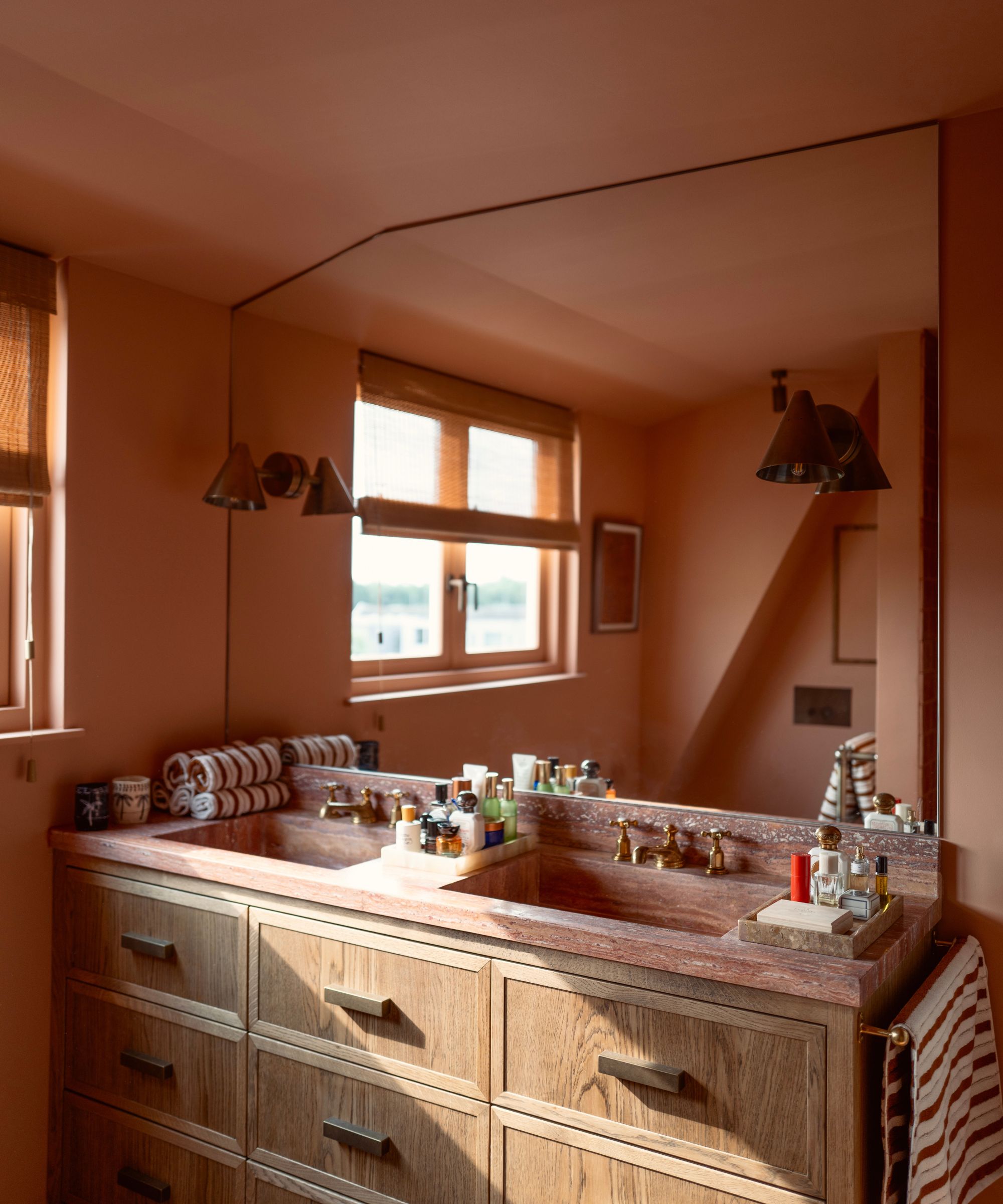 Bathroom with Naperon by Farrow &amp;amp; Ball painted walls, a wooden double vanity unit with a red marble top, and a large mirror with two brass sconces on either side.