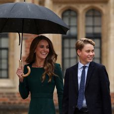 Princess Kate smiling and holding an umbrella with Prince George