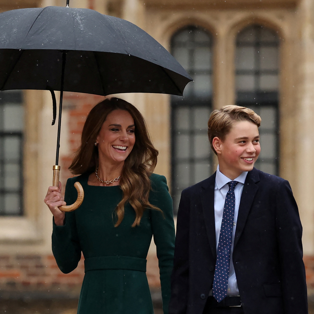 Princess Kate smiling and holding an umbrella with Prince George