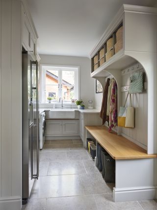 A bright utility room featuring a window above a large sink, a fridge and a wooden bench