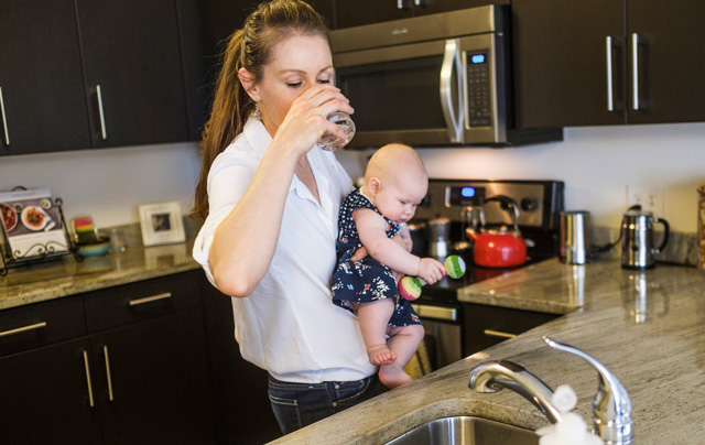 Women on breastfeeding diet holding her baby and drinking water in the kitchen