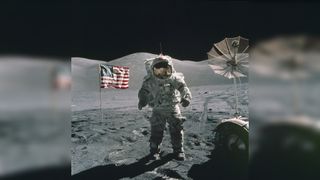 An Apollo 17 astronaut stands on the lunar surface with the United States flag in the background.