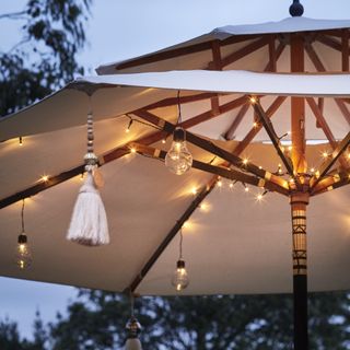 An example of outdoor string lighting ideas showing a garden parasol with string lights