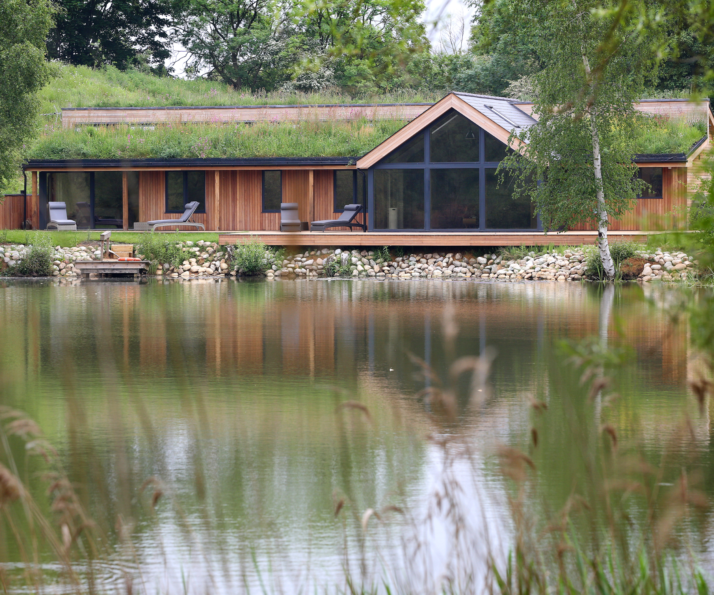 single storey timber clad house with large glazed gable end and grass roof