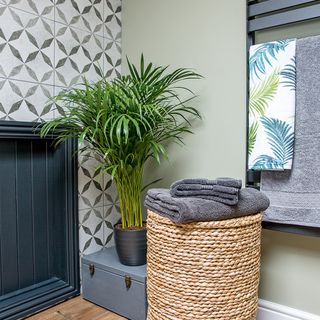 Stack of grey towels on top of a wicker laundry basket in a green and grey bathroom