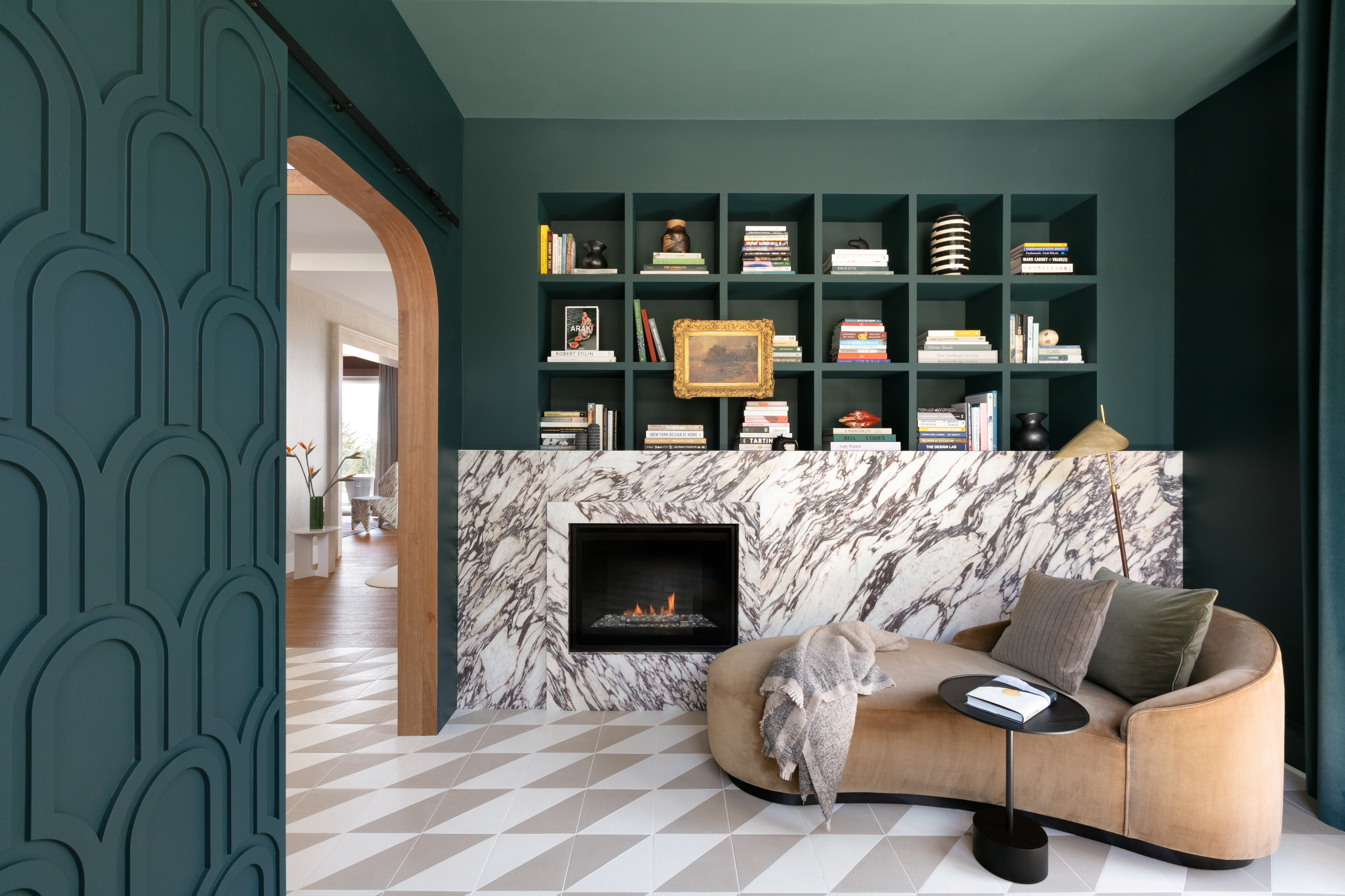 A corner in a living room with a large, marble fireplace, and an open built in bookshelf behind it