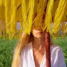 Summer perfumes: a woman stands under a yellow sun shade in a meadow