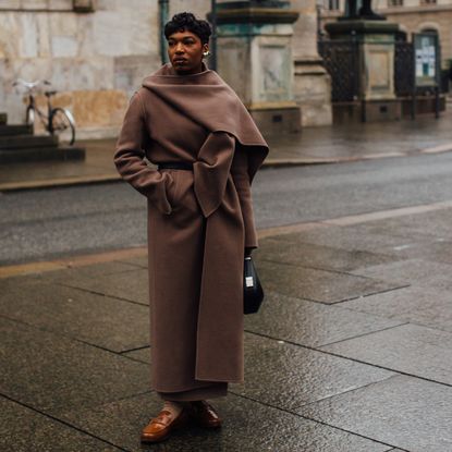 Woman wearing long brown coat with built-in scarf and brown loafers