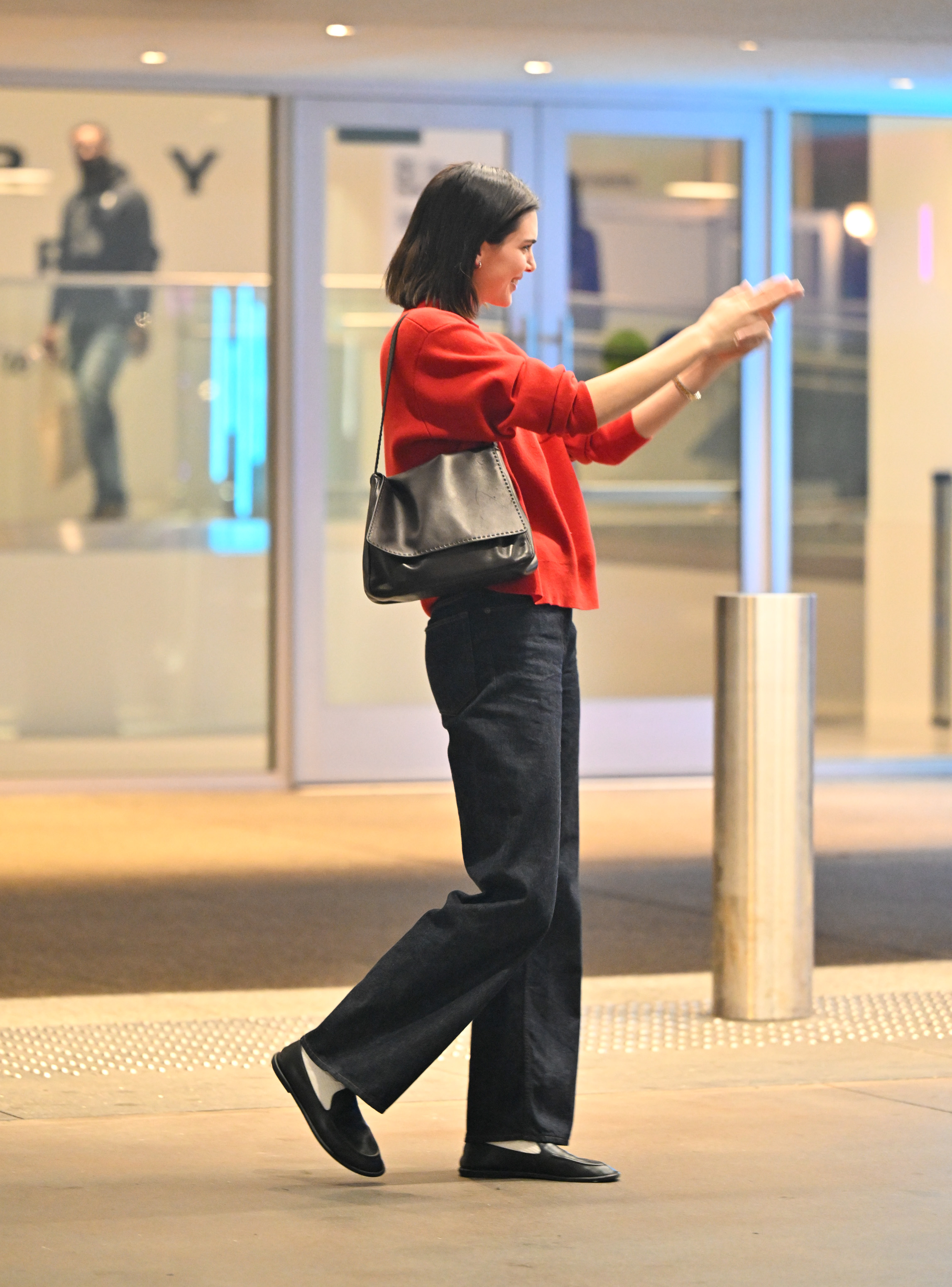 Kendall Jenner wears a red sweater, black shoulder bag, black jeans, white socks, and black The Row loafers.