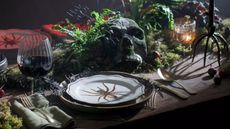 Halloween tablescape with moss decor, ribbed wine glasses, spider candle holders, matching plates, and sage green linen napkins