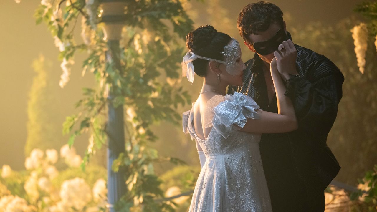 A masked man (Luke Thompson as Benedict Bridgerton) kisses a masked woman&#039;s (Yerin Ha as Sophie Baek) hand as they stand outdoors, in &#039;Bridgerton&#039; season 4.