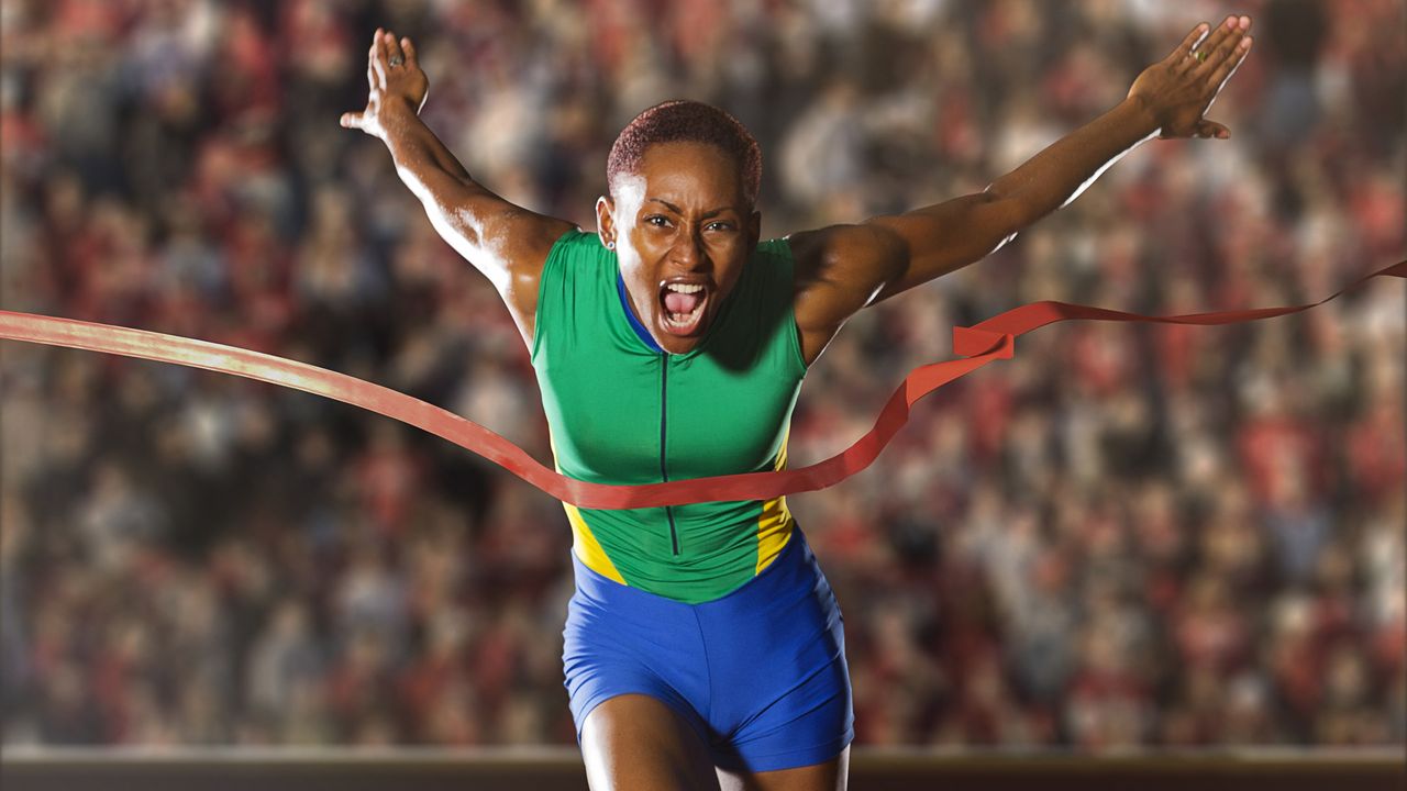 A runner looks intense as she breaks through the tape at the finish line of a race. 