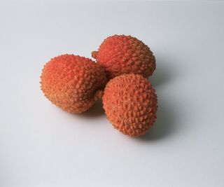 Three red ripe lychee fruit on a white background