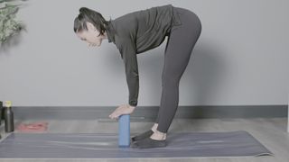 Sam Hopes performing forward fold on yoga mat with hands on yoga block