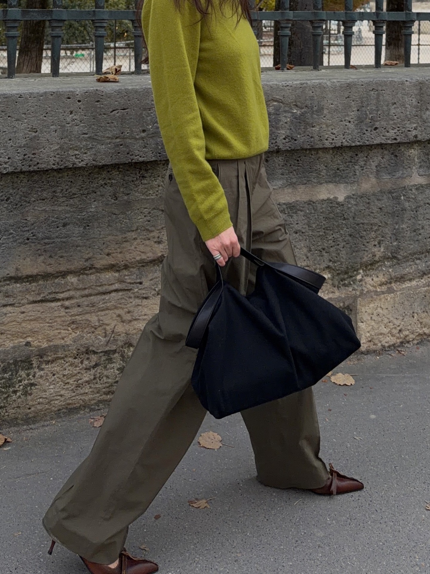 Annabel wears a green sweater, green trousers, a black bag, and brown pumps.