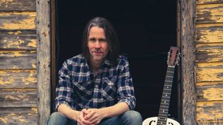 Myles Kennedy sitting in a doorway with a banjo