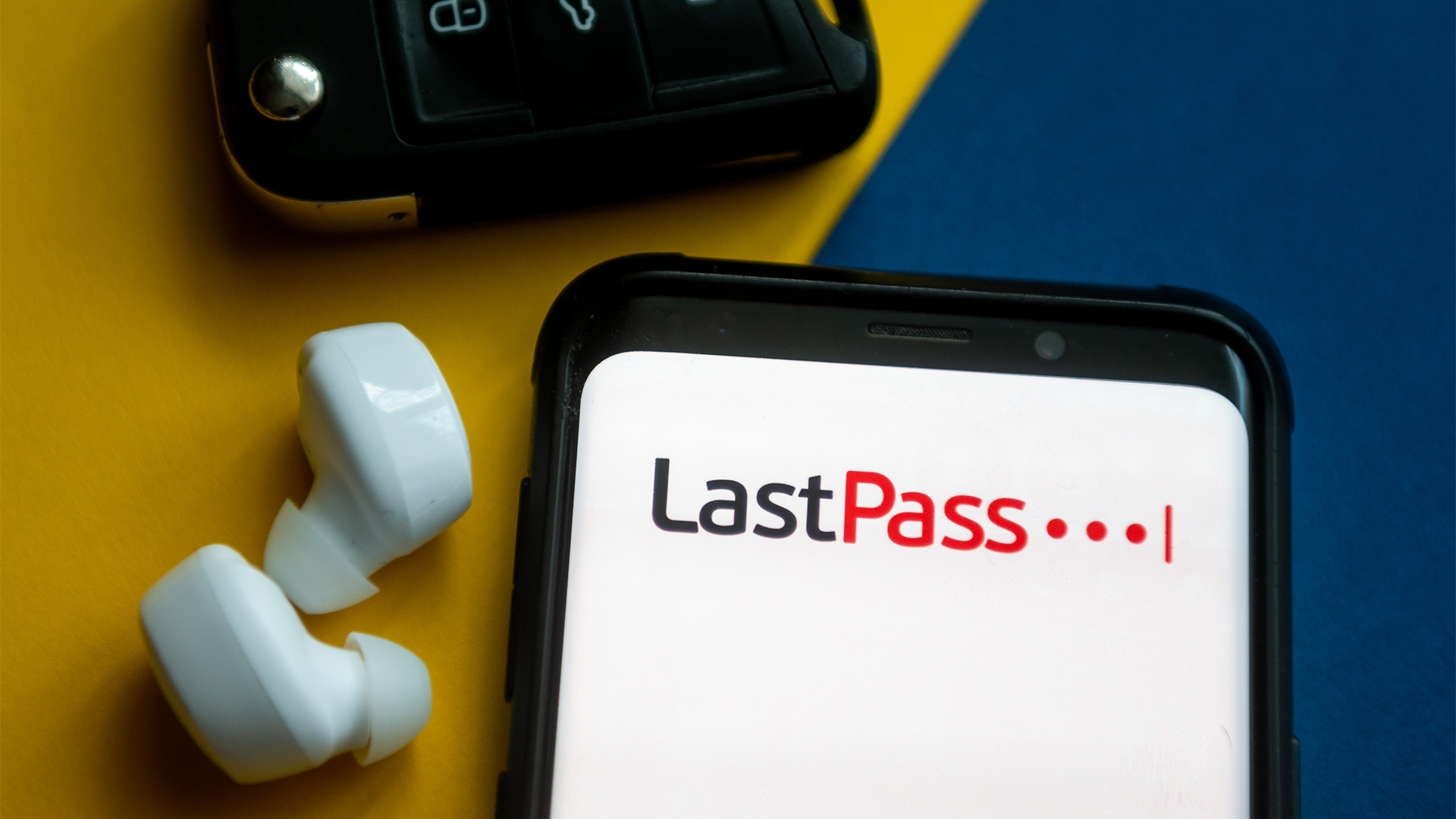 LastPass logo pictured on a smartphone screen alongside earbuds and car key.