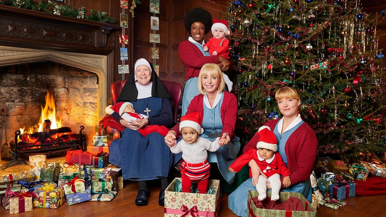 Sister Monica Joan (Judy Parfitt) and midwives Joyce, Trixie, and Rosalind play with young babies in Santa outfits in the very festively decorated interior of Nonnatus House, in a promo shot for the Call the Midwife 2025 Christmas special.