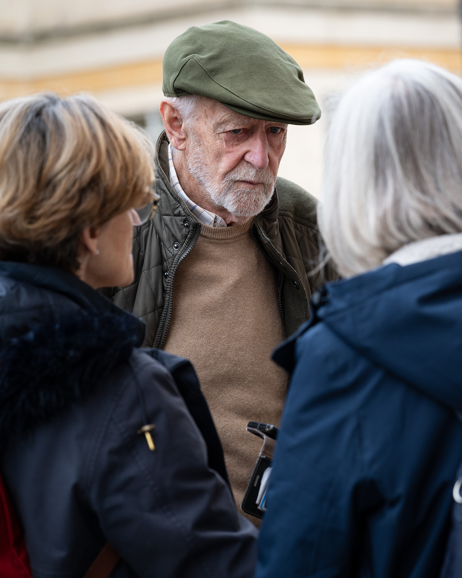 Street photograph of man with flat cap talking to two women