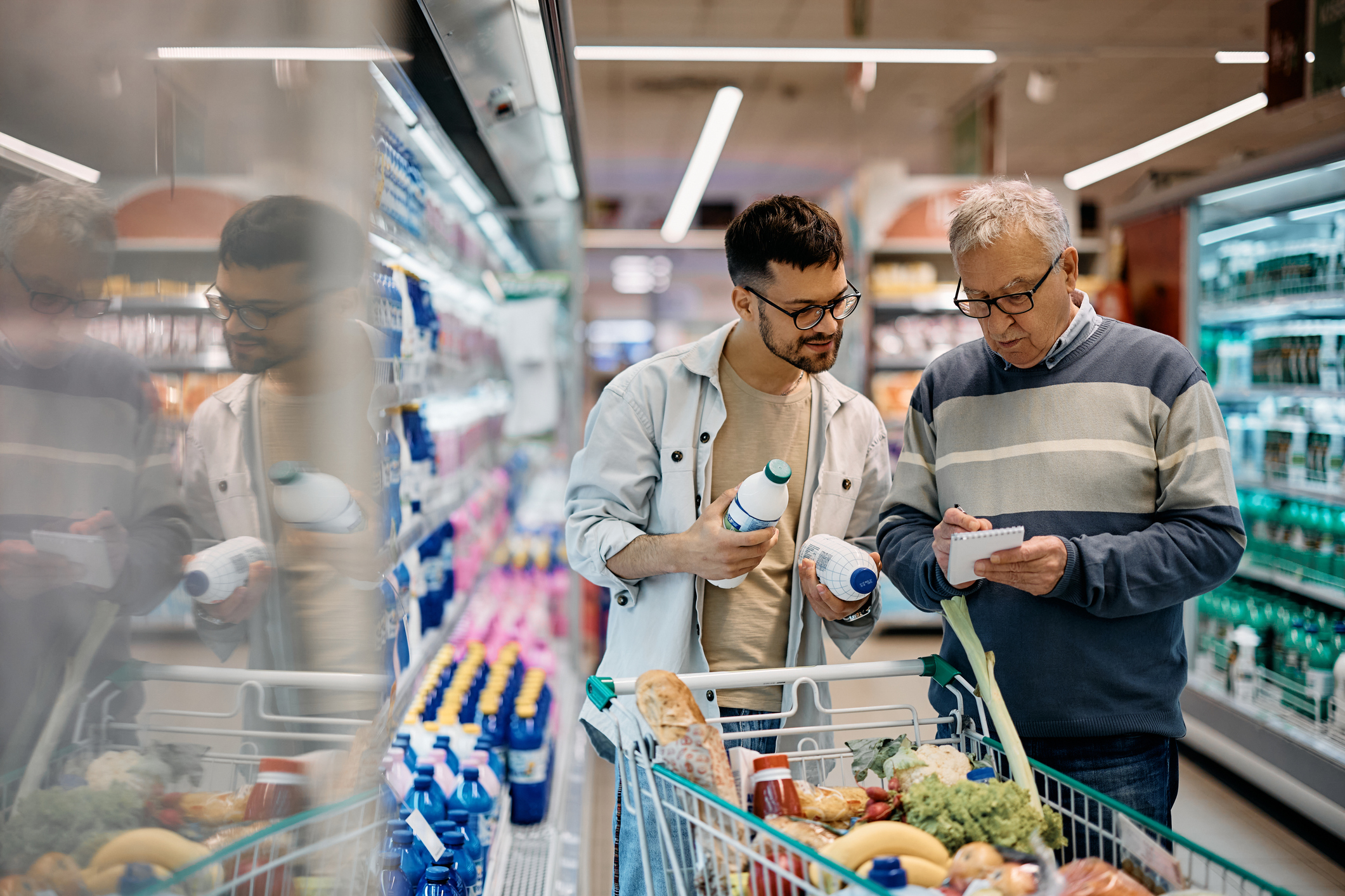 Young man and his senior father going through shopping list while buying in supermarket