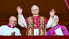 Pope Leo XIV stands in papal robes in the middle of two other men on the Vatican loggia