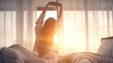 Woman stretches as she gets out of bed in front of the sunrise