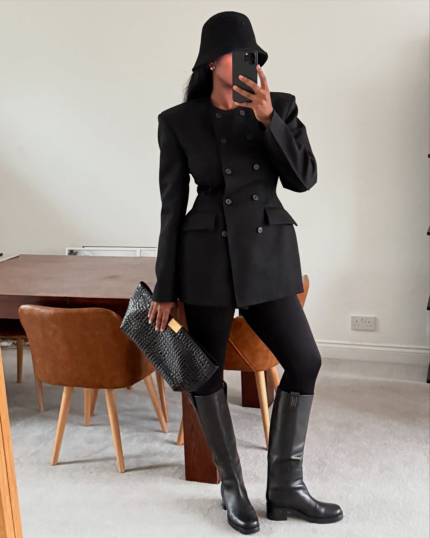 An image of @nlmarilyn wearing leather riding boots with a waisted dress and wool bucket hat, one of the biggest trends to wear with leggings in 2026.