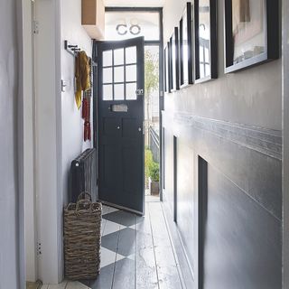 A narrow white and grey hallway with stencilled floorboards and big grey door