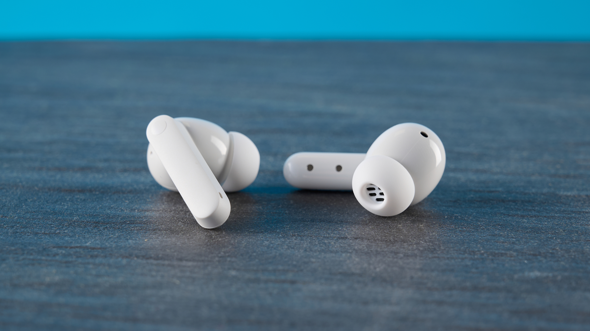 CMF Buds 2 Plus in light gray photographed in front of a blue background