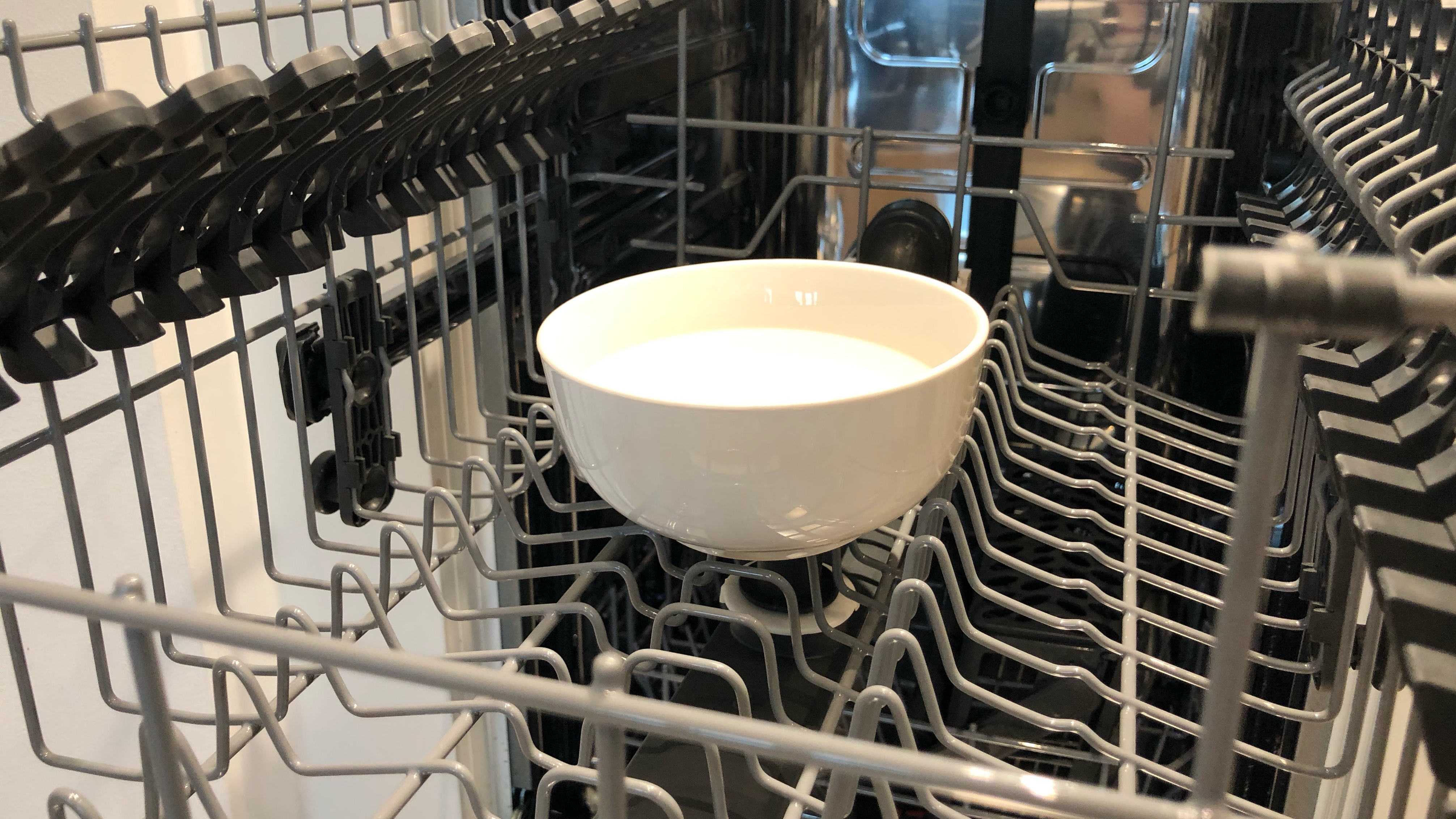 A bowl of vinegar situated on the top rack of a dishwasher to clean the dishwasher of limescale