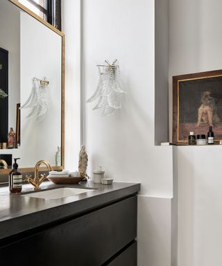A white bathroom with a glamorous light fitting and a wooden vanity