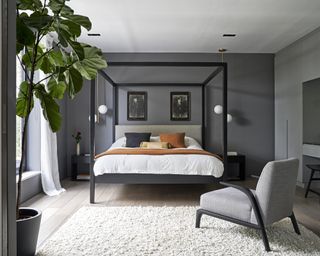 A bedroom with dark gray walls and a black, contemporary four poster bed