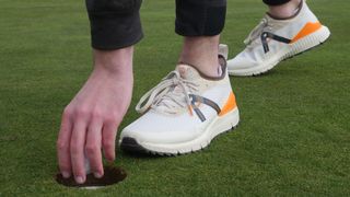Dan Parker picking up a ball from a golf hole testing the Cole Haan ZeroGrand Overtake golf shoe