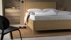 IKEA N&Auml;STABERG Mattress topper on a pine double bed in a neutral taupe bedroom with black chair, jute rug, and bathroom drawers and circular mirror seen behind.
