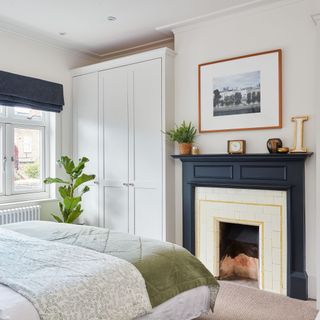 Bedroom with grey bedding, fitted wardrobe and open fireplace with blue/black surround