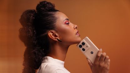 A person holding the Motorola Edge 50 Ultra on an orange background