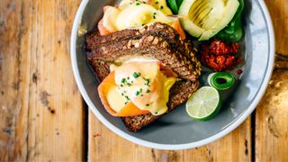 Bowl of whole grain bread with salmon, poached eggs and avocado sitting on wooden table