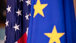 Flags of the United States and European Union pictured together, with EU flag in foreground blurred and US flag in background.