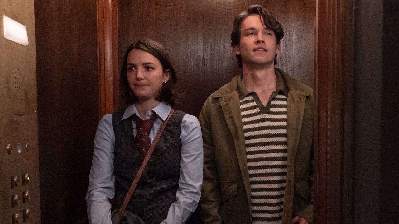 Ella Hunt and Jack Martin standing together in an elevator looking in opposite directions. 