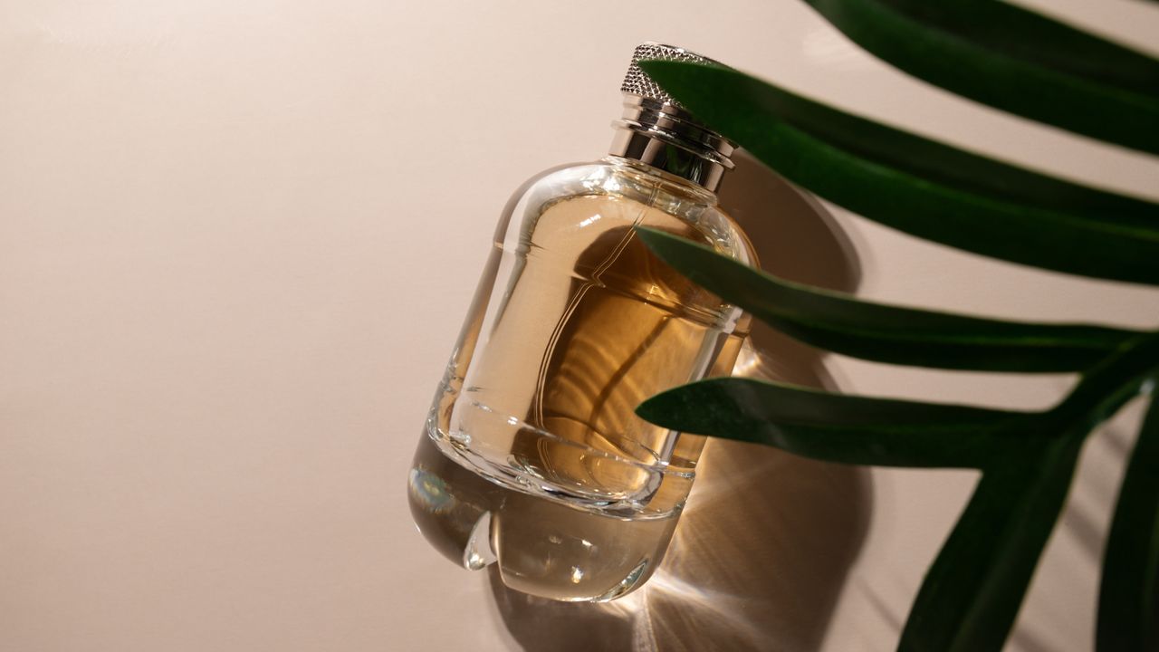 Golden perfume with palm leaf on beige background, glamorous glass bottle, luxurious packaging