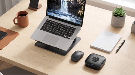 A clean home office desk with a laptop on a stand, a mouse, a notebook, and conference speaker. And, of course, an all-important mug of coffee