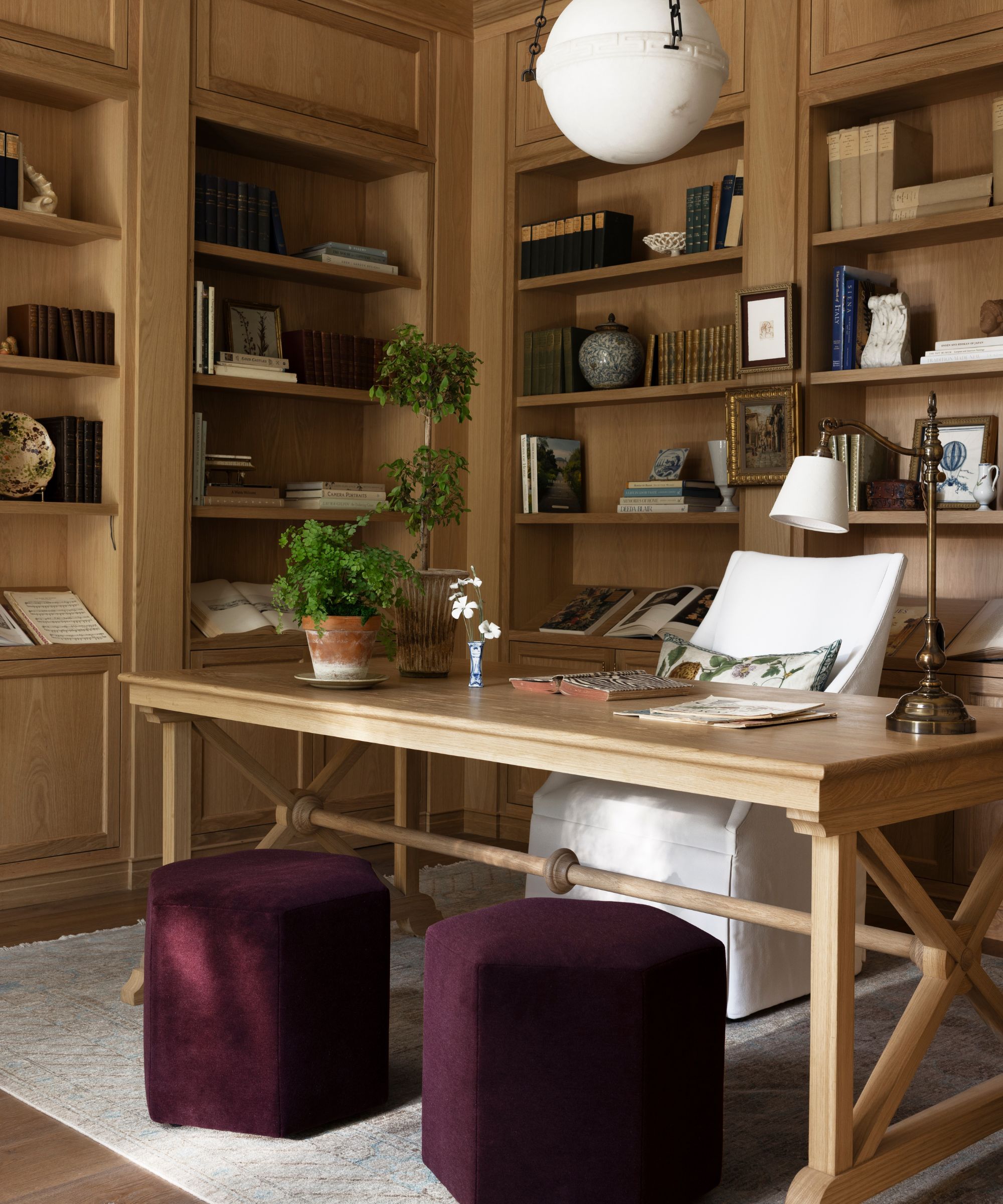 a home office clad in oak bookcases with an oak trestle style desk with white chair and two small purple stools